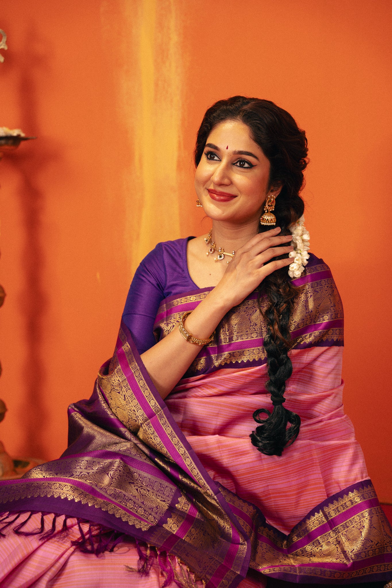 Woman in a pink and purple vintage Kanchipuram silk saree with gold accents against an orange background