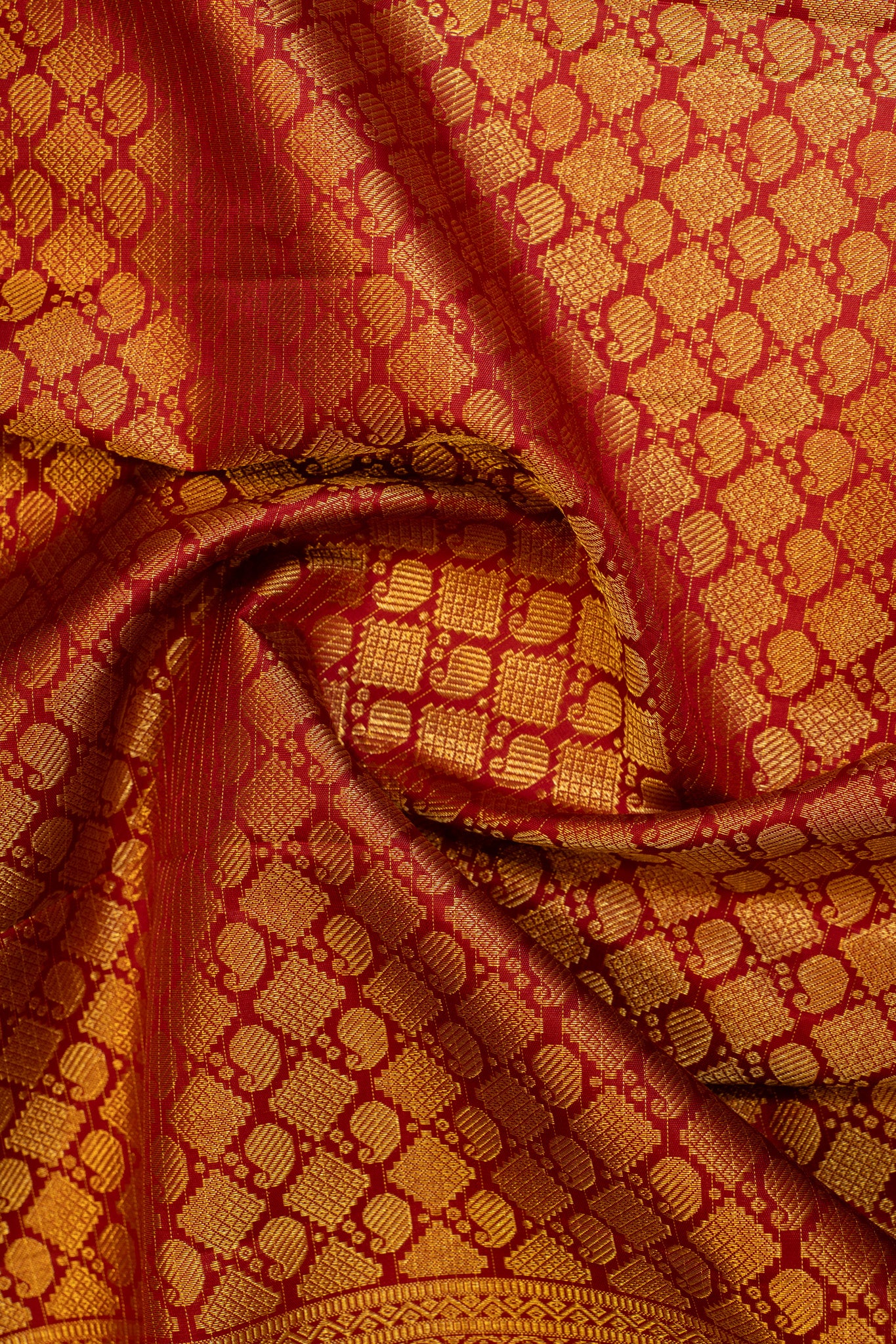 Detailed shot of the pallu of a traditional maroon and off white Kanjivaram silk saree, adorned with gold zari motifs