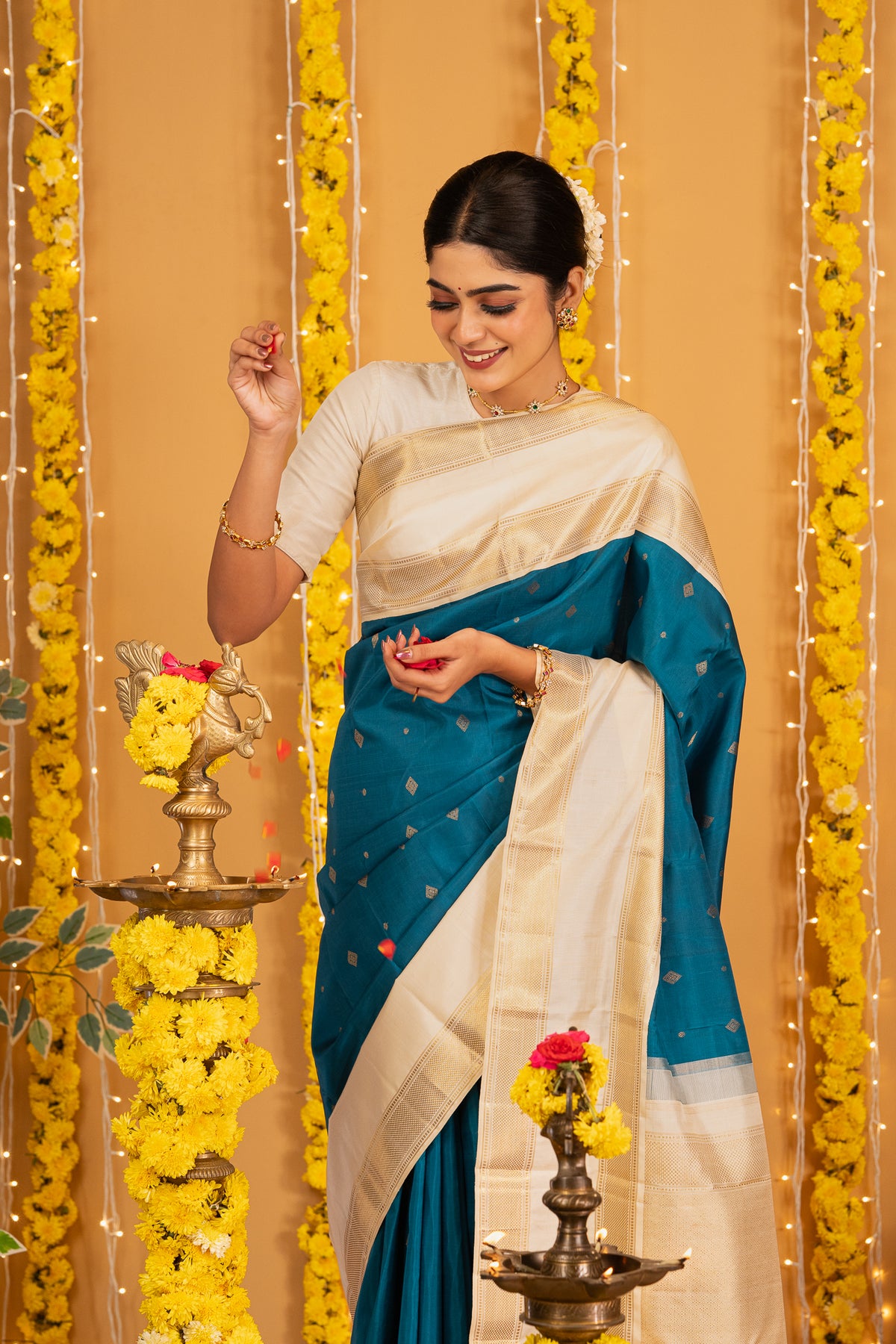 Woman in a yellow and brown saree performing a traditional ritual with a brass lamp.